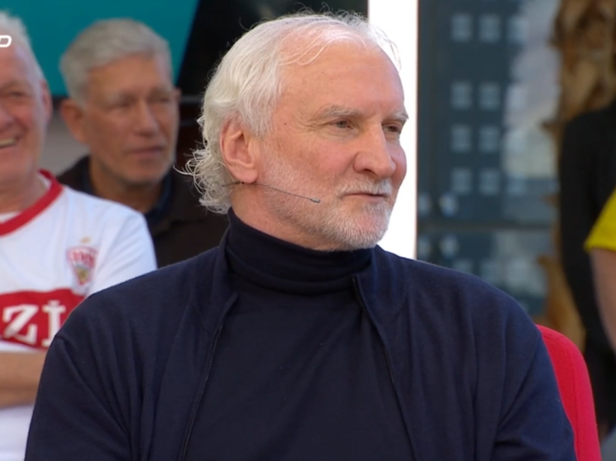 Rudi Völler sitzt mit Rollkragen-Pullover im „Doppelpass“.