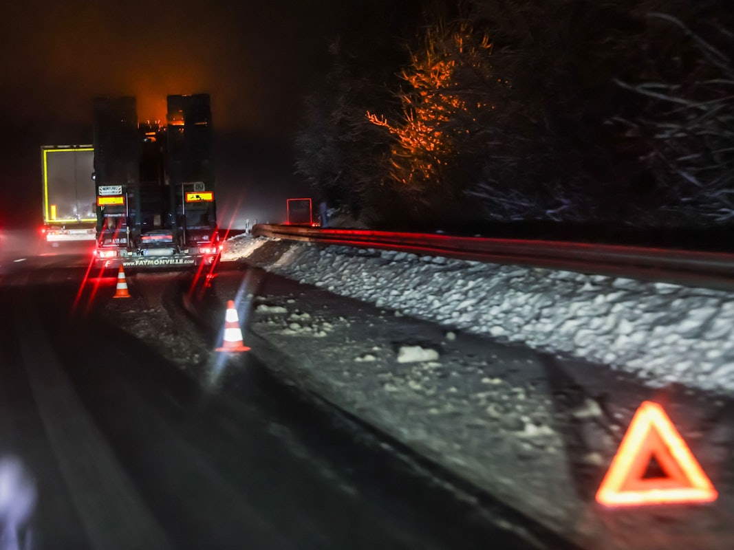 Ein Lkw steht im Dunkeln an einem schneebedeckten Straßenrand, davor ein Warndreieck.