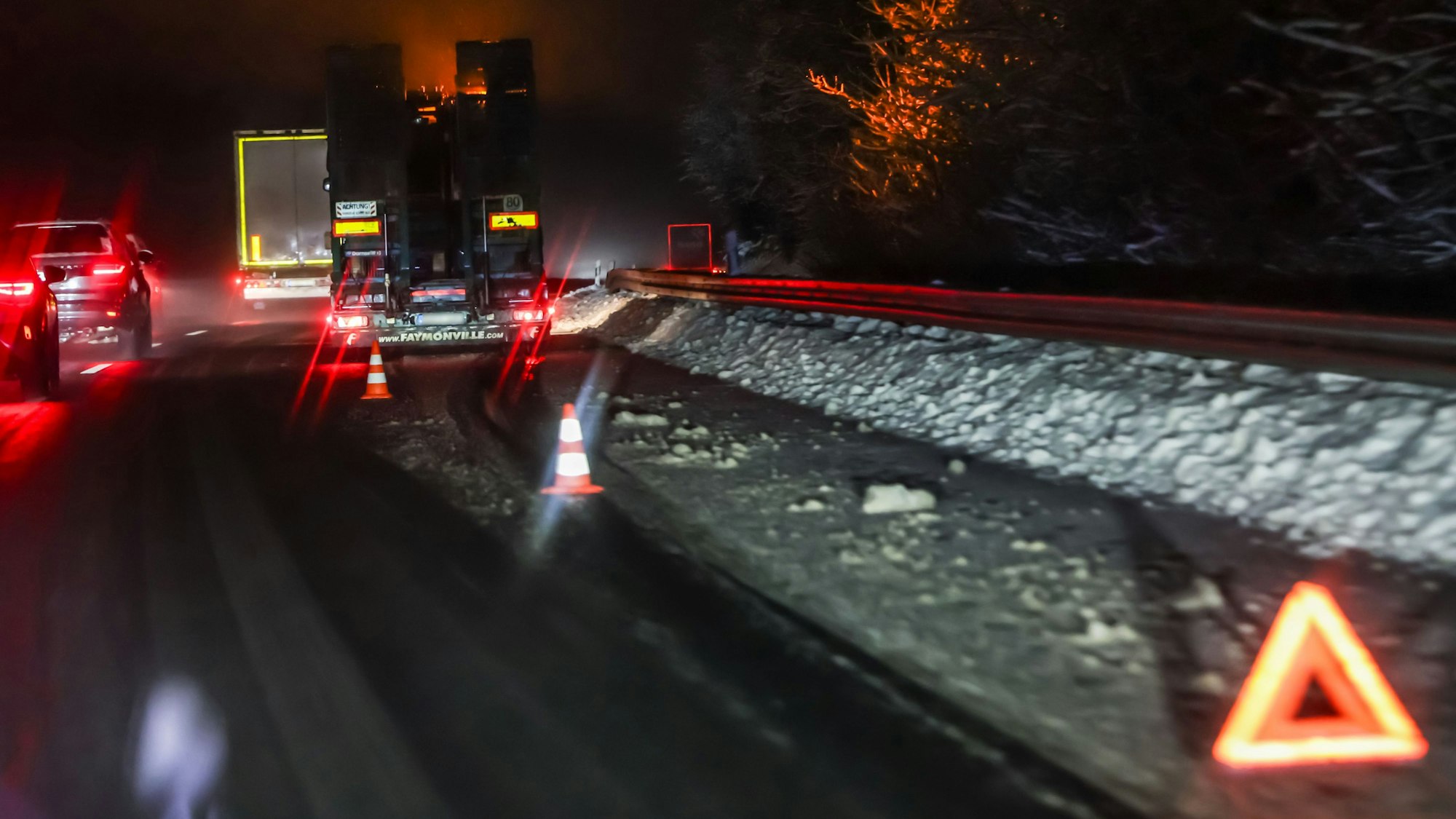 Ein Lkw steht im Dunkeln an einem schneebedeckten Straßenrand, davor ein Warndreieck.