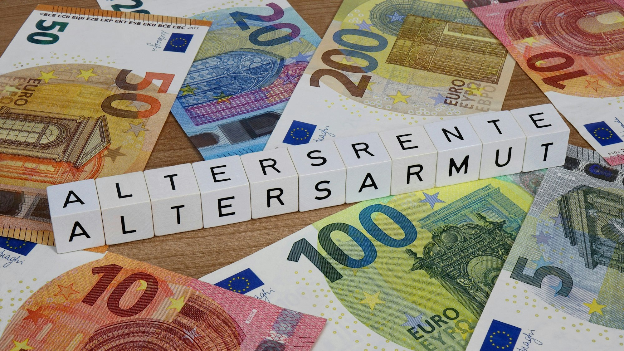 Geldscheine und Buchstabenwürfel bilden Altersrente Altersarmut