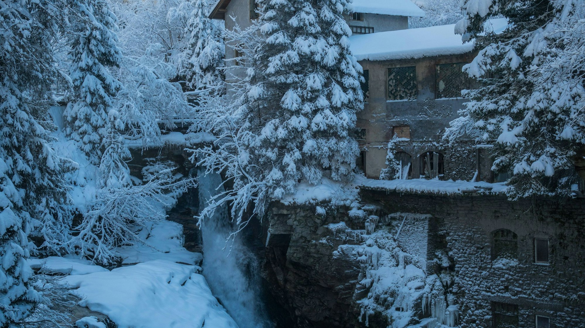 Schneebedeckte Winterlandschaft mit Wasserfall und Gebäuden