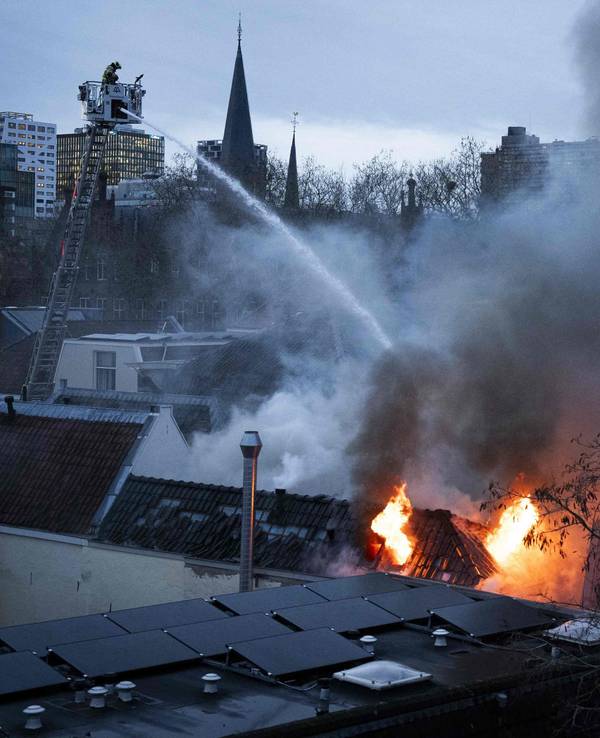 Ein Feuerwehrmann steht auf einer Drehleiter und löscht von oben ein brennendes Gebäude.