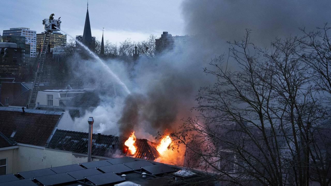 Ein Feuerwehrmann steht auf einer Drehleiter und löscht von oben ein brennendes Gebäude.