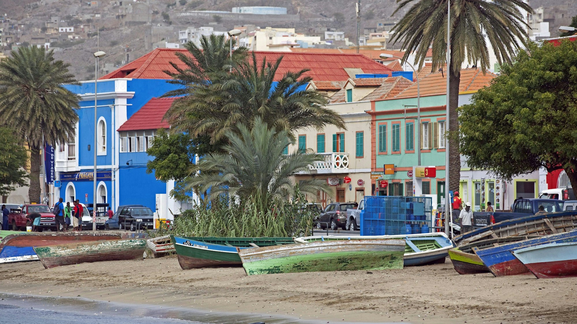 Fischerboote aus Holz liegen am Strand entlang einer Uferpromenade.