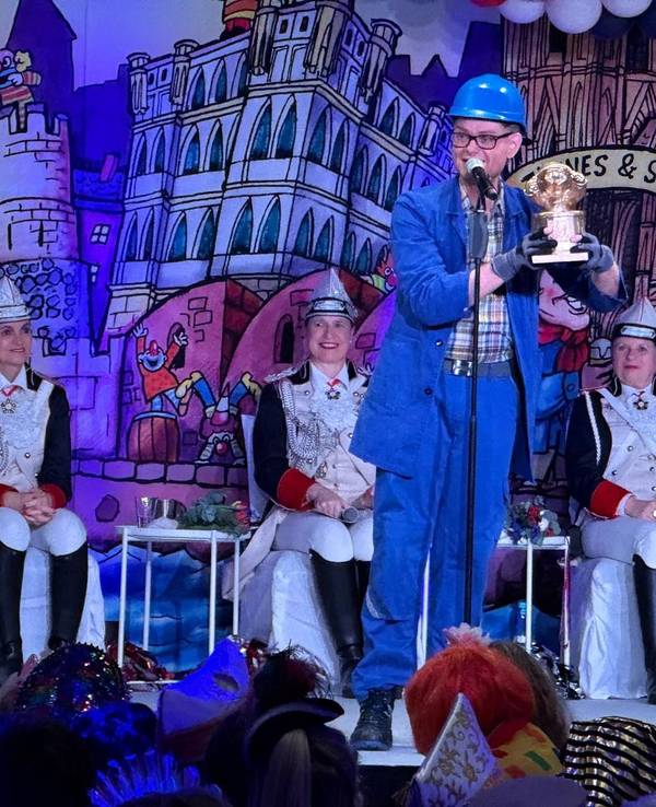 Handwerker Peters steht mit Trophäe auf der Bühne.