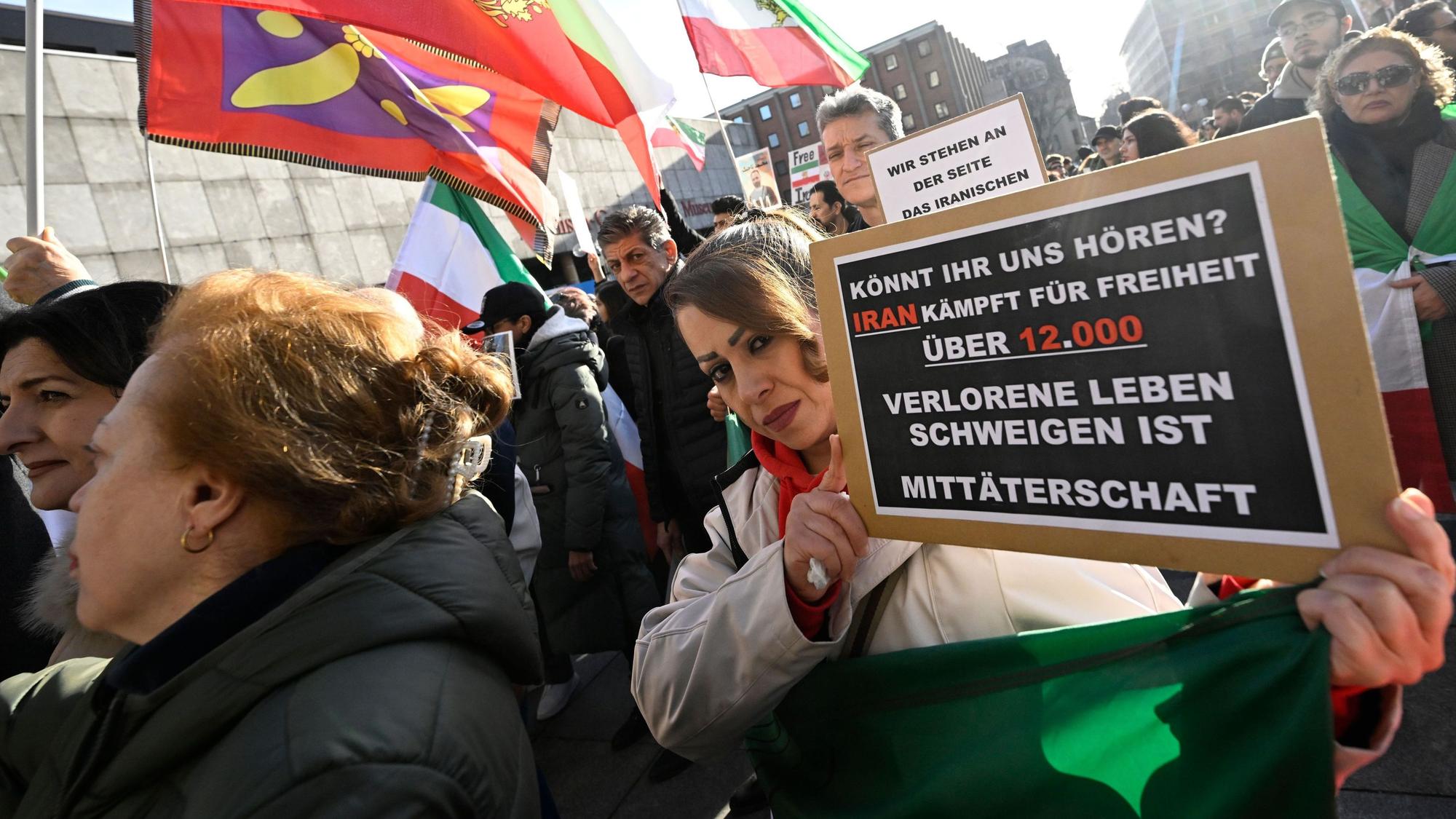 Teilnehmer halten bei einer Demonstration Schilder und Fahnen zur Unterstützung der Proteste im Iran.