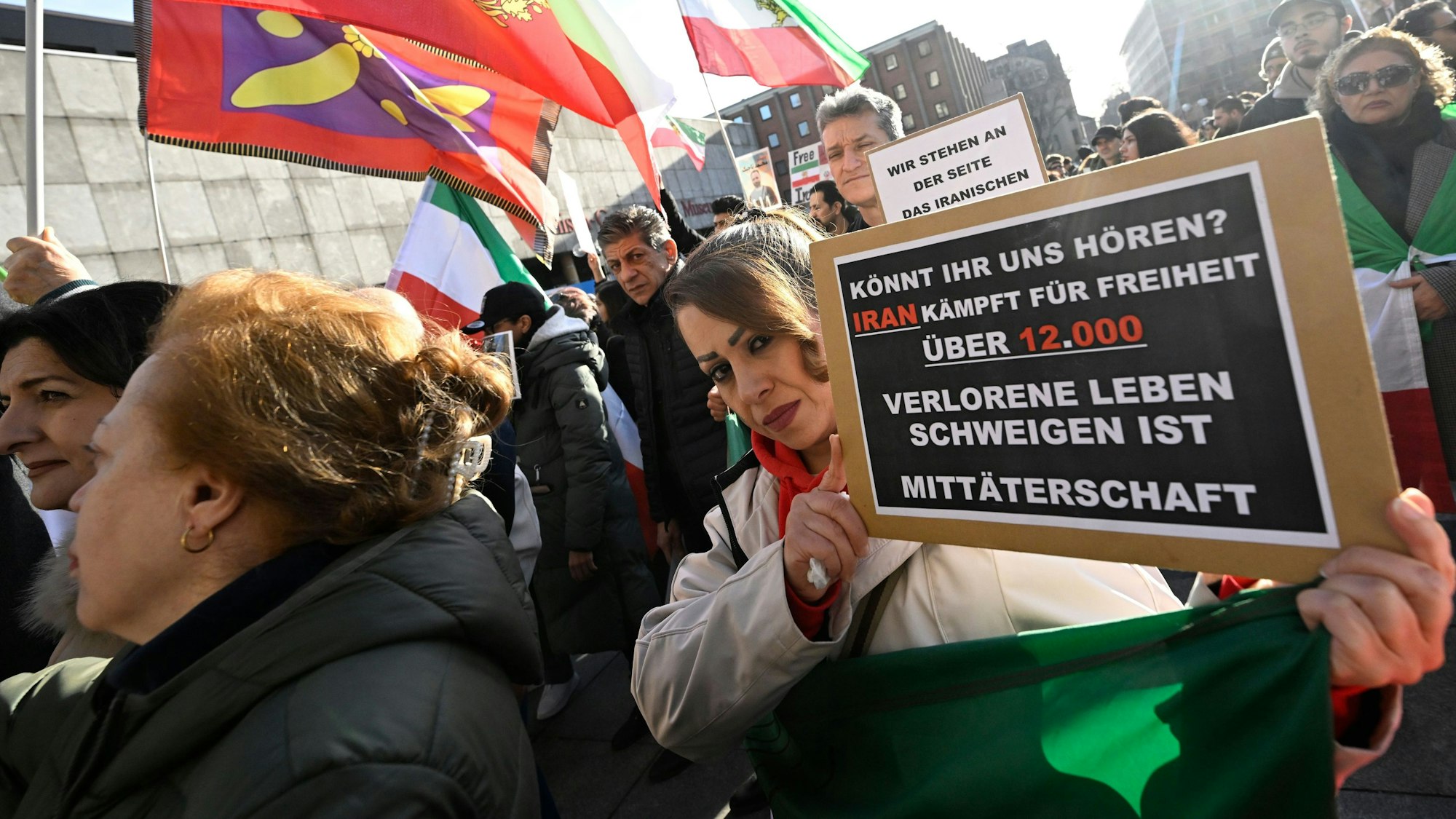Teilnehmer halten bei einer Demonstration Schilder und Fahnen zur Unterstützung der Proteste im Iran.