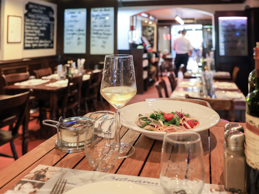 In einem Restaurant stehen auf einem Tisch ein Teller Nudeln und ein Weinglas.