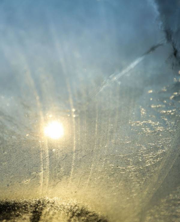Die Sonne scheint durch die vereiste Windschutzscheibe eines PKW.