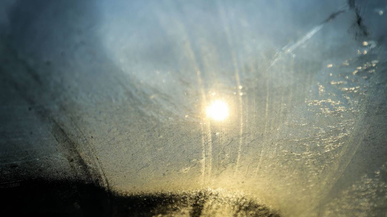 Die Sonne scheint durch die vereiste Windschutzscheibe eines PKW.