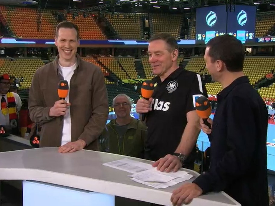 Alfred Gislason steht zwischen Moderater Florian Zschiedrich und Experte Sven-Sören Christophersen. Allre grinsen.