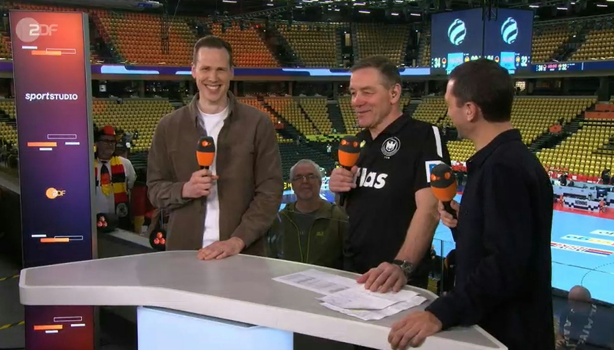 Alfred Gislason steht zwischen Moderater Florian Zschiedrich und Experte Sven-Sören Christophersen. Allre grinsen.