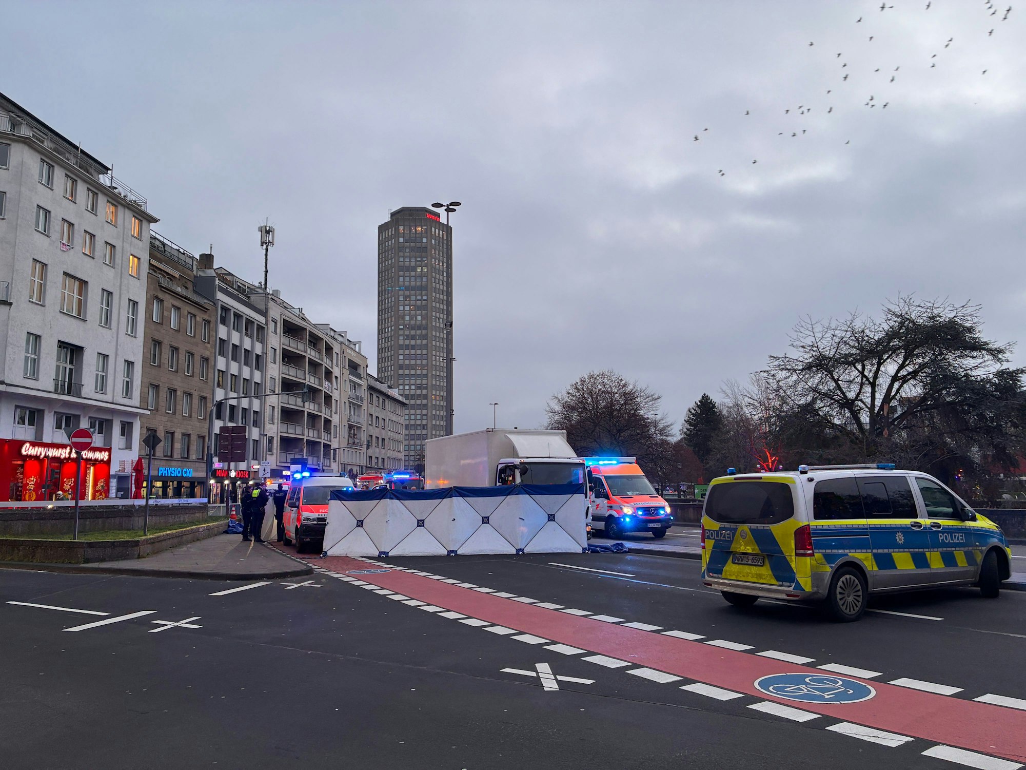 Die Polizei hat auf einer Fahrbahn einen Sichtschutz errichtet, davor stehen ein Lkw sowie Einsatzfahrzeuge von Polizei und Rettungsdienst.