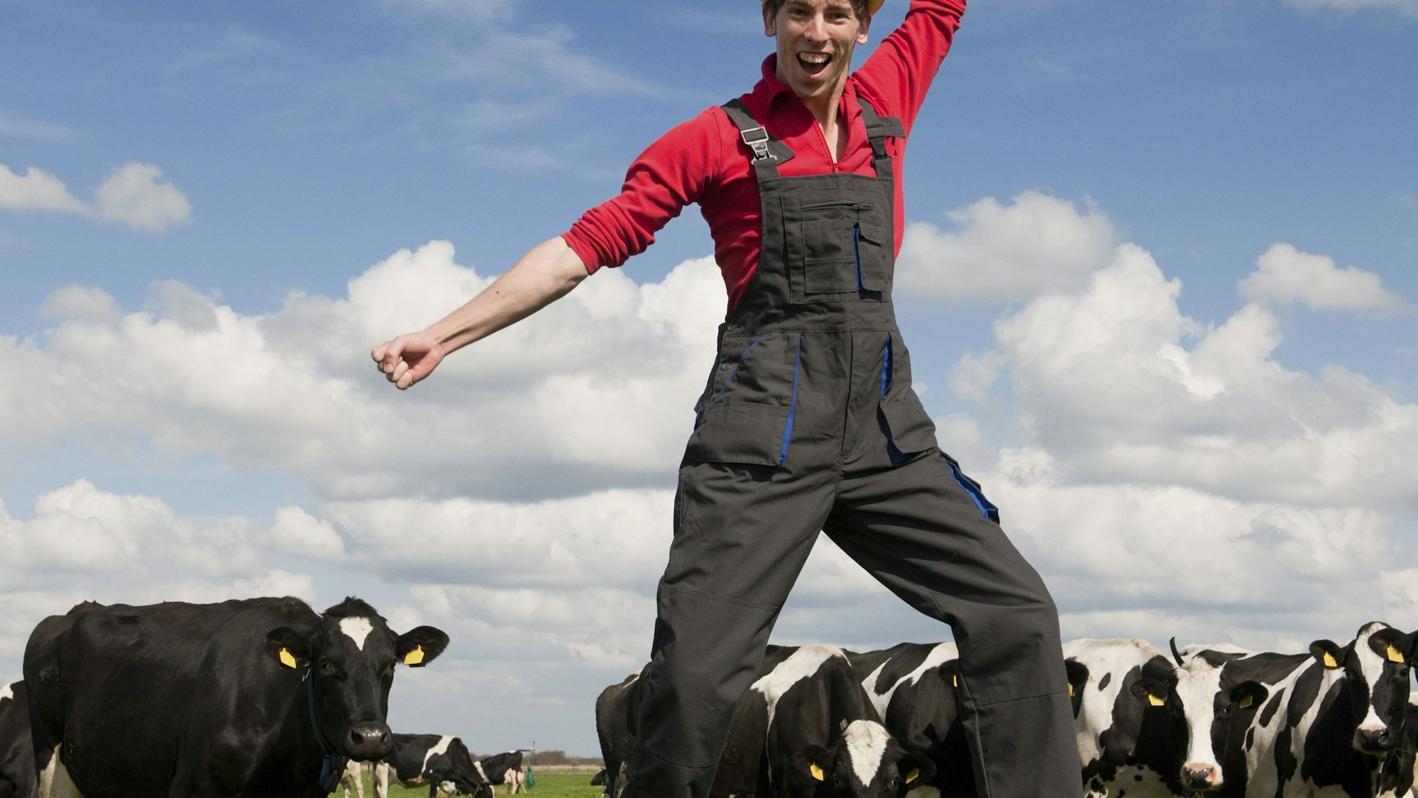 Junger Bauer springt auf Feld mit Kühen