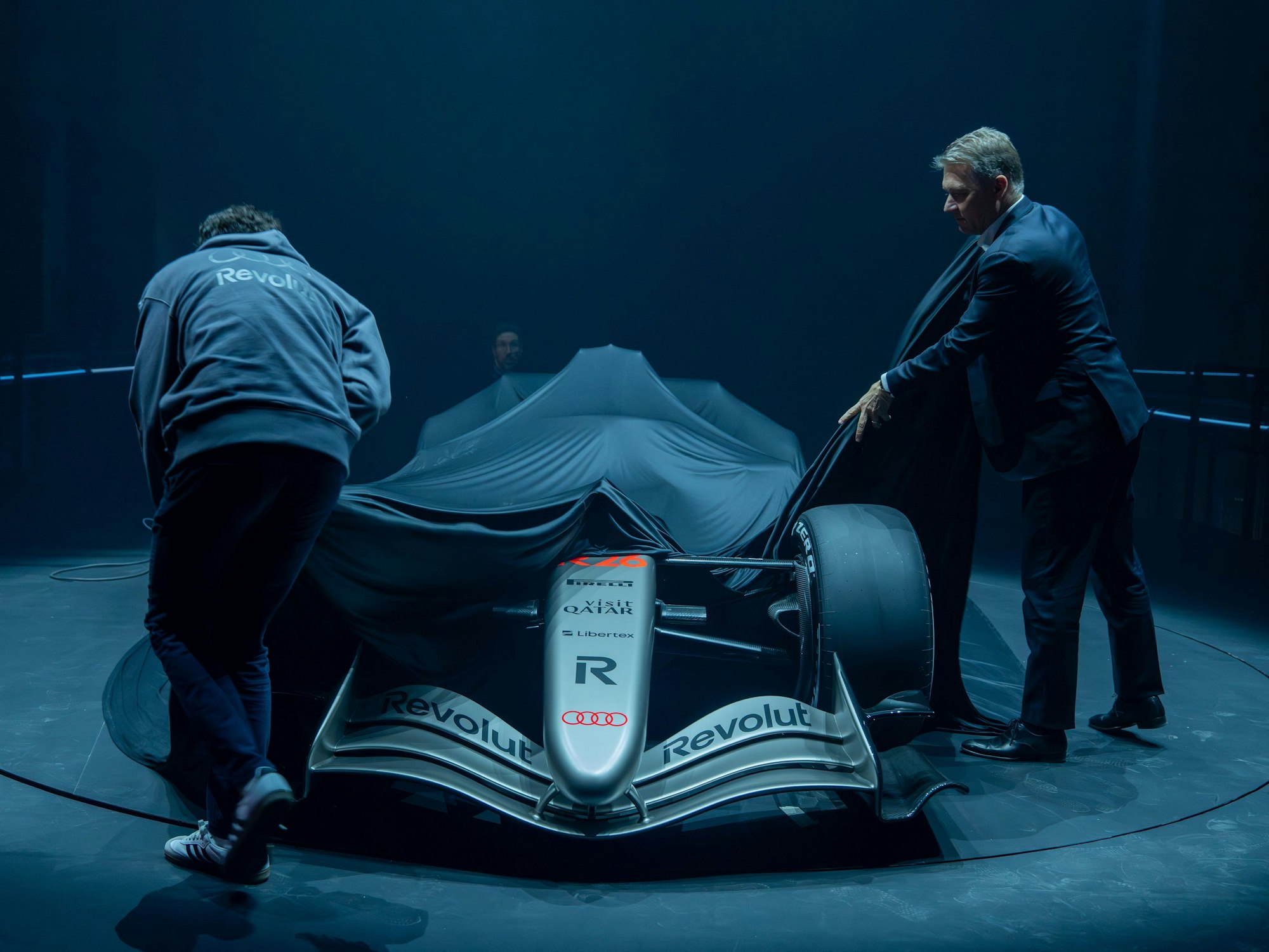 Gernot Döllner (r), Vorstandsvorsitzender der Audi AG, und ein Mitarbeiter ziehen die Plane von dem Formel-1-Rennwagen R 26 von Audi Revolut, der während der Vorstellung des Fahrzeuges im Kraftwerk Mitte auf einer Bühne steht.