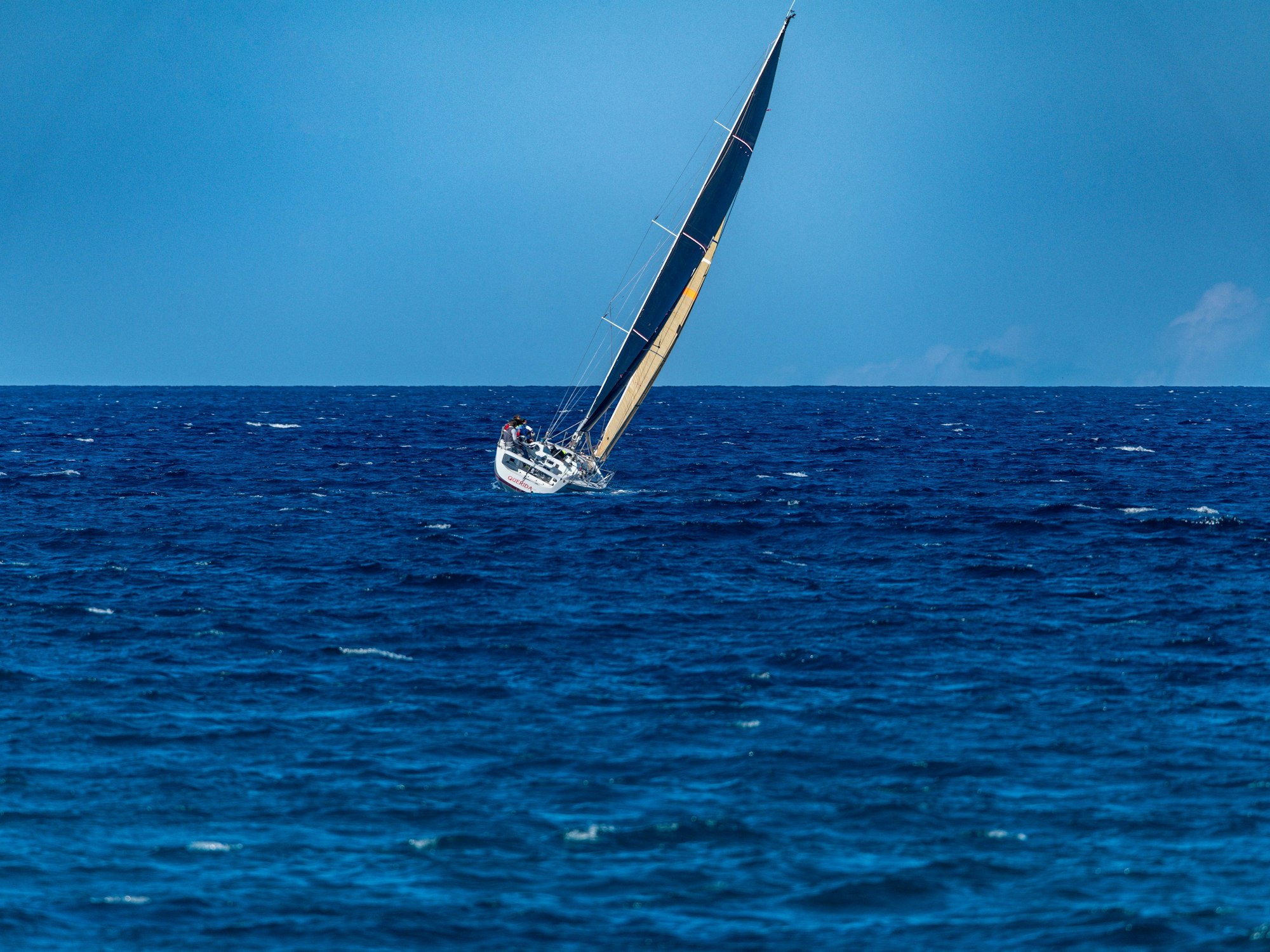 Eine Segelyacht lehnt sich bei klarem Himmel auf offener See in den Wind.