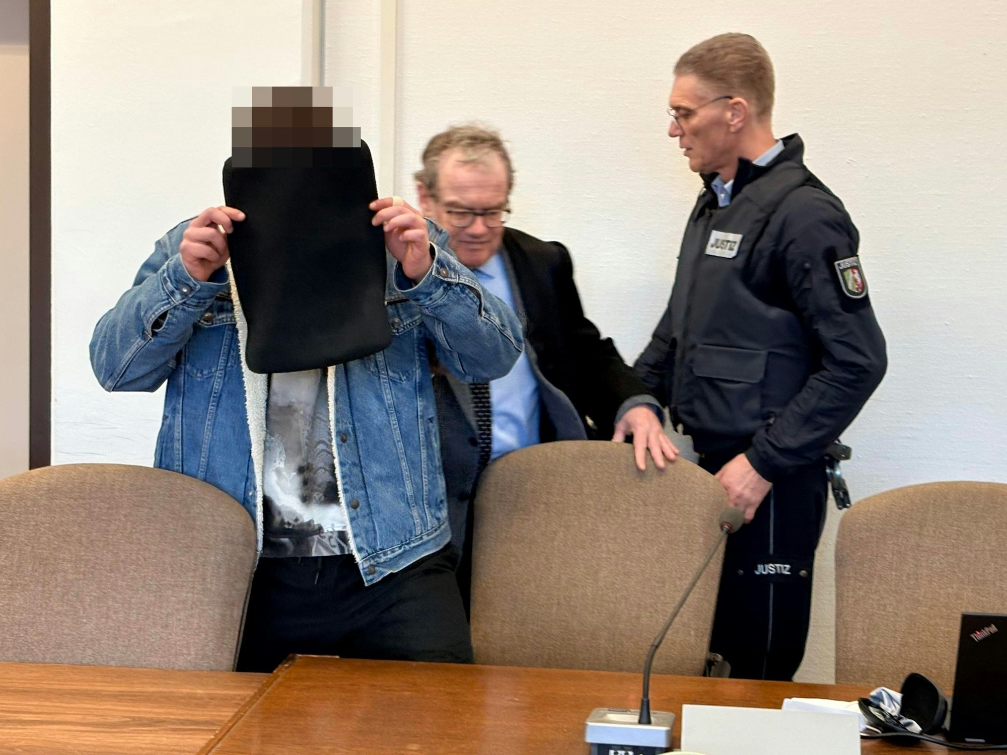Der Angeklagte mit seinem Verteidiger Lukas Pieplow und einem Wachtmeister beim Prozessauftakt im Kölner Landgericht.