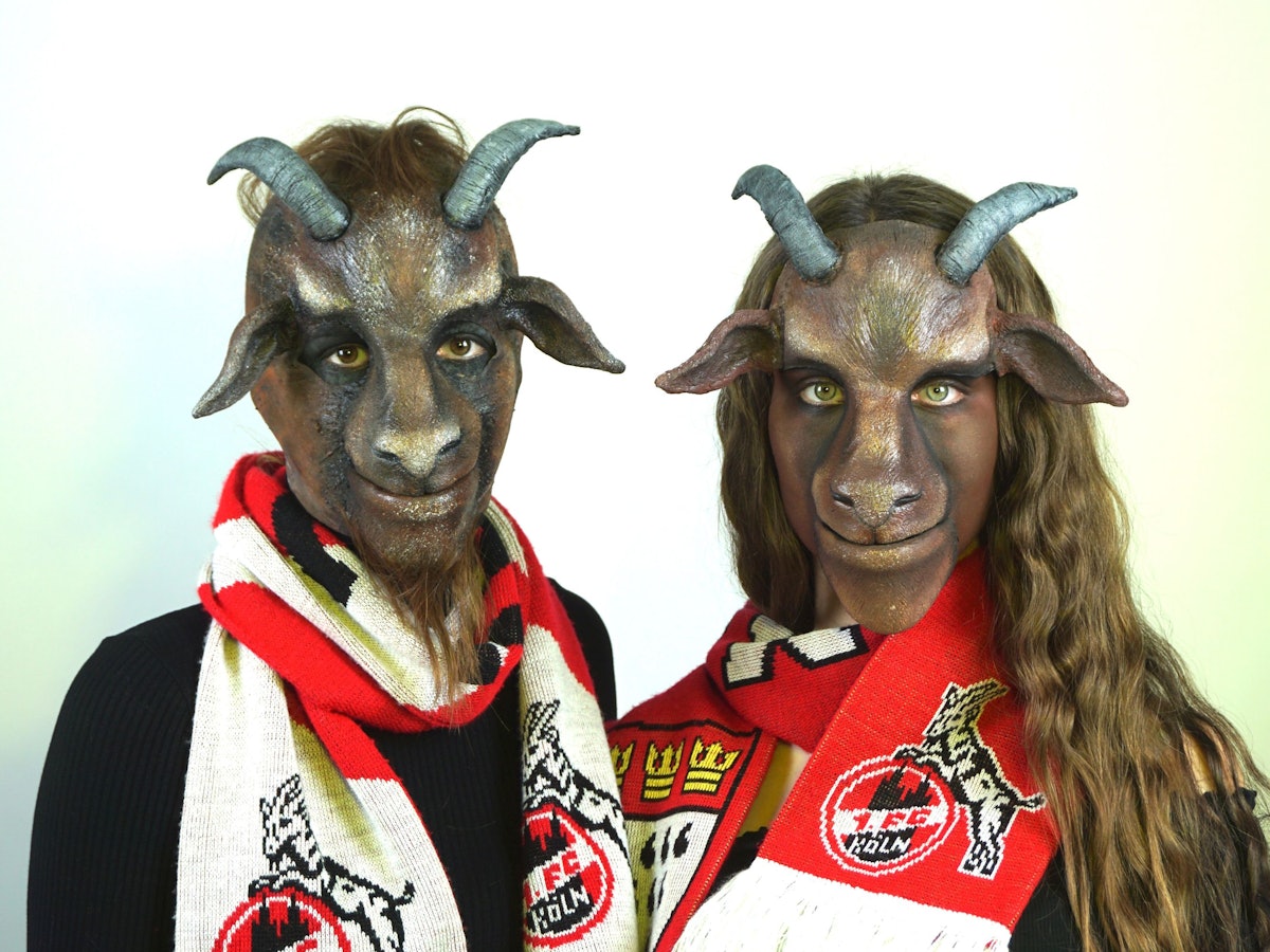 Zwei als Ziegenbock geschminkte Personen mit Schals des 1. FC Köln um den Hals und künstlichen Hörnern auf dem Kopf.