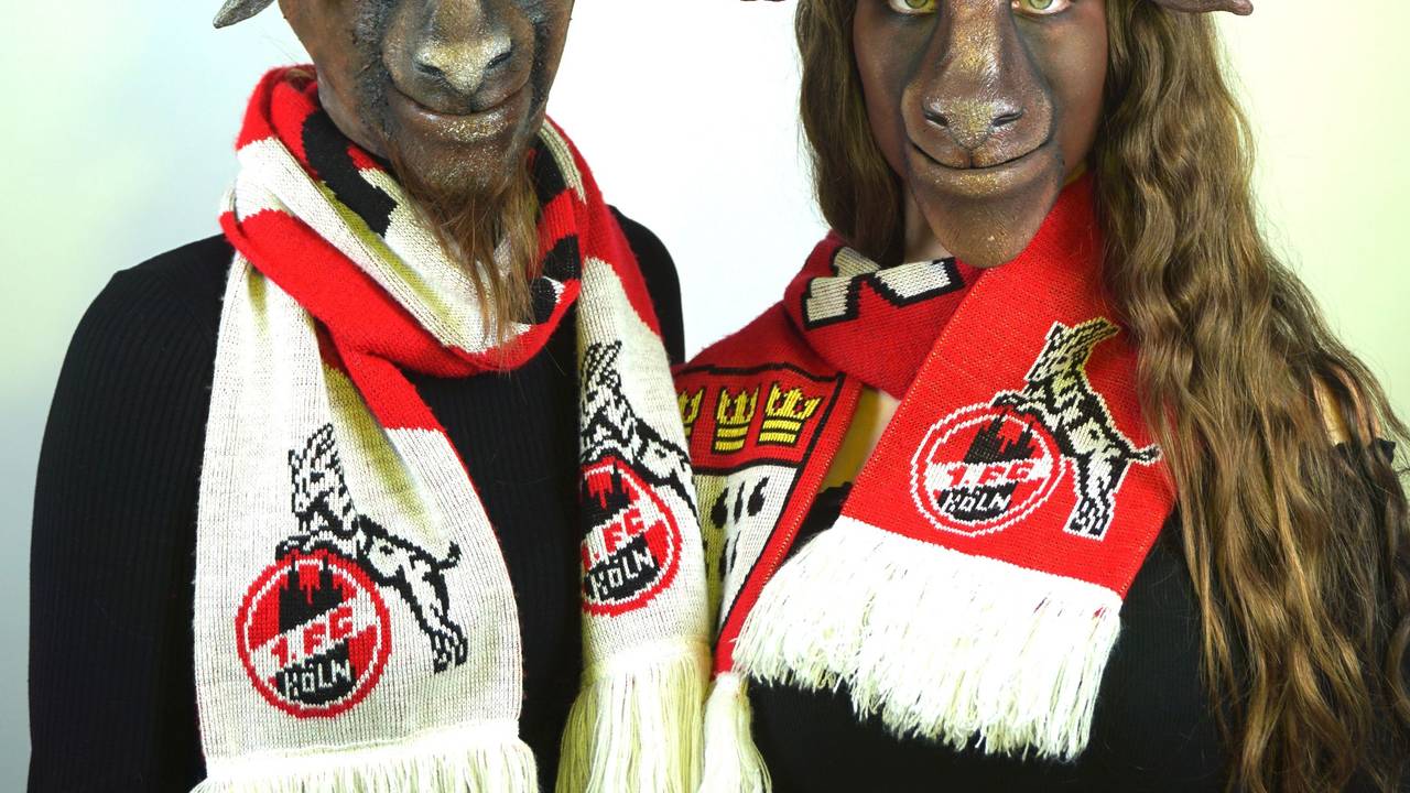 Zwei als Ziegenbock geschminkte Personen mit Schals des 1. FC Köln um den Hals und künstlichen Hörnern auf dem Kopf.