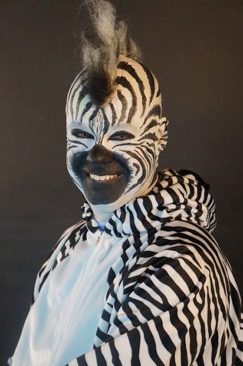 Eine als Zebra geschminkte und verkleidete Person lacht in die Kamera