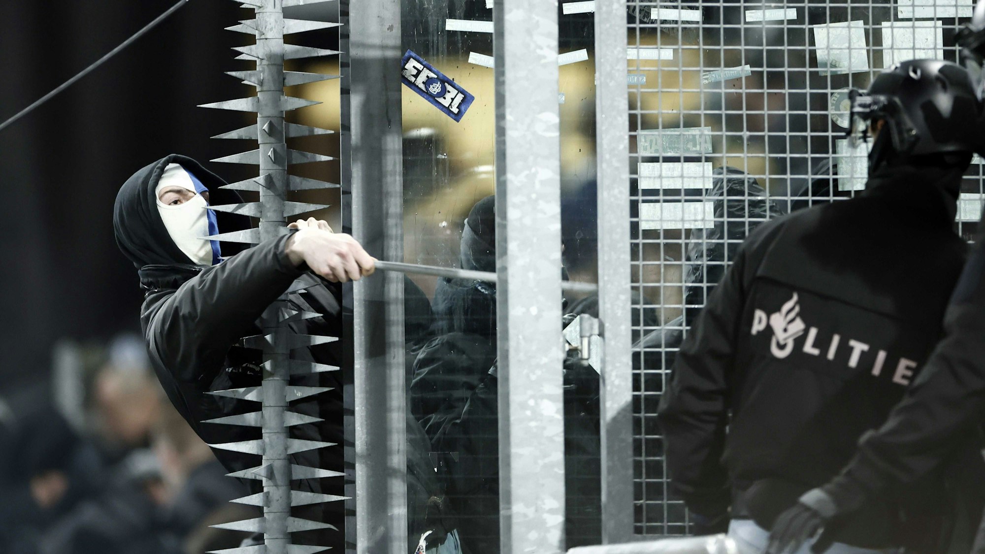 Ein maskierter Fan von Genk schlägt mit einer Eisenstange nach einem Polizisten.