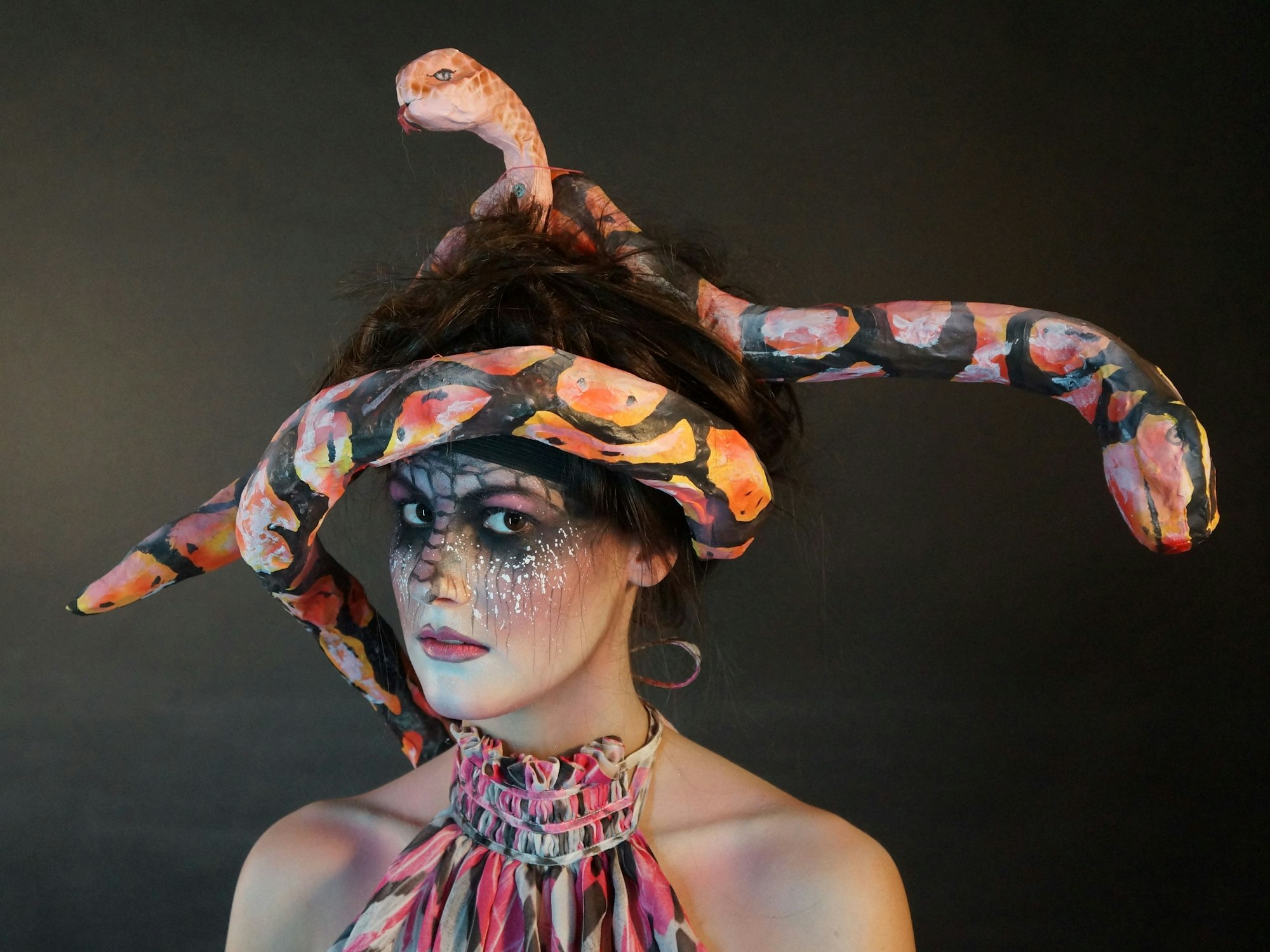 Eine Frau ist als Schlange geschminkt und trägt eine Pappmaché-Schlange auf dem Kopf