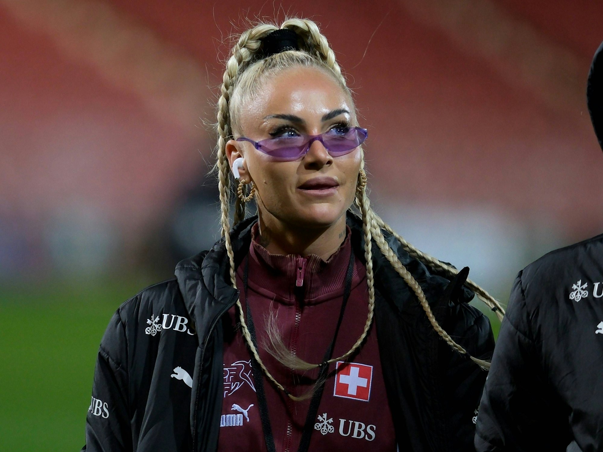 Alisha Lehmann vor einem Spiel der Schweizer Nationalmannschaft. Sie trägt eine schmale lilafarbene Brille auf der Nase und hat Kopfhörer in den Ohren.