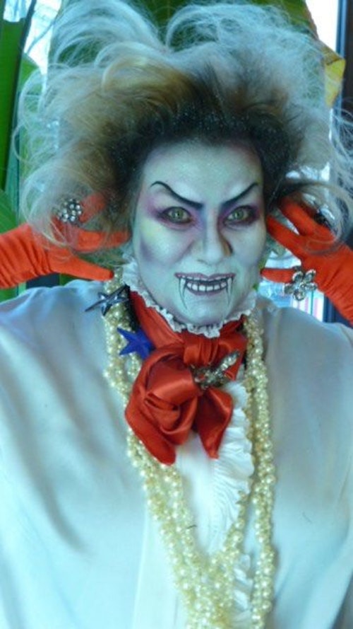 Eine Frau mit wirrer Perücke ist als kalkweißer und gruseliger Vampir geschminkt