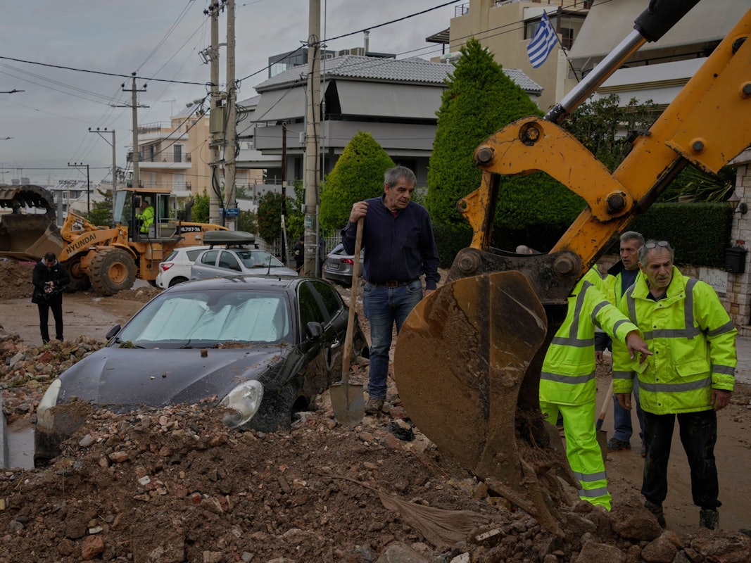 Städtische Arbeiter und Anwohner befreien eine Straße neben einem beschädigten Auto von Schlamm und Trümmern, nachdem es im Athener Stadtteil Glyfada zu Überschwemmungen gekommen ist.