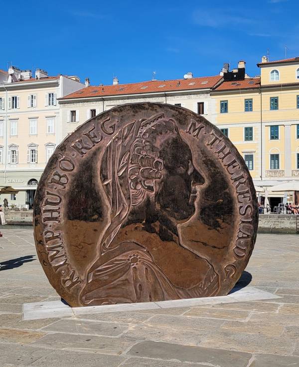 Eine überdimensionale Münze mit dem Konterfei Maria Theresias darauf steht auf einem Platz zwischen alten Häusern