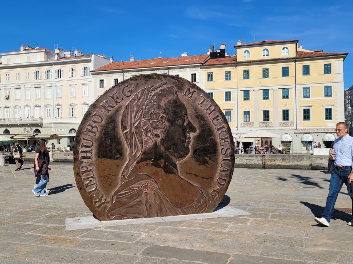 Eine überdimensionale Münze mit dem Konterfei Maria Theresias darauf steht auf einem Platz zwischen alten Häusern