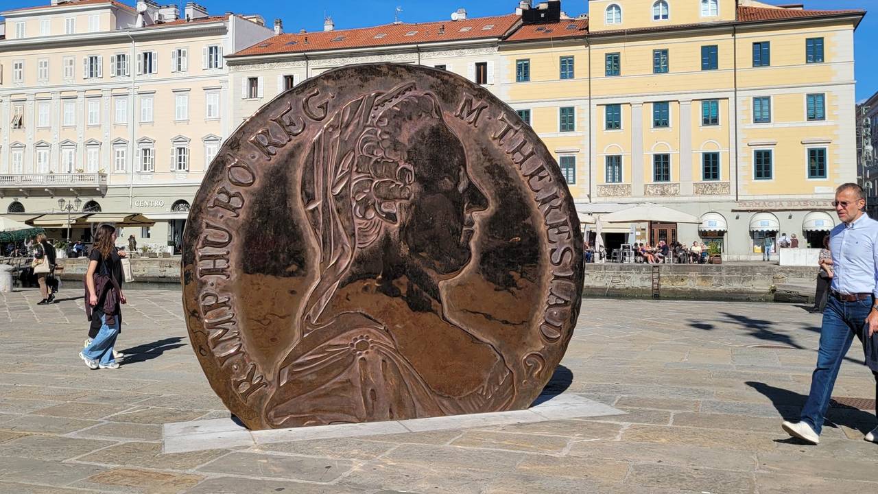 Eine überdimensionale Münze mit dem Konterfei Maria Theresias darauf steht auf einem Platz zwischen alten Häusern