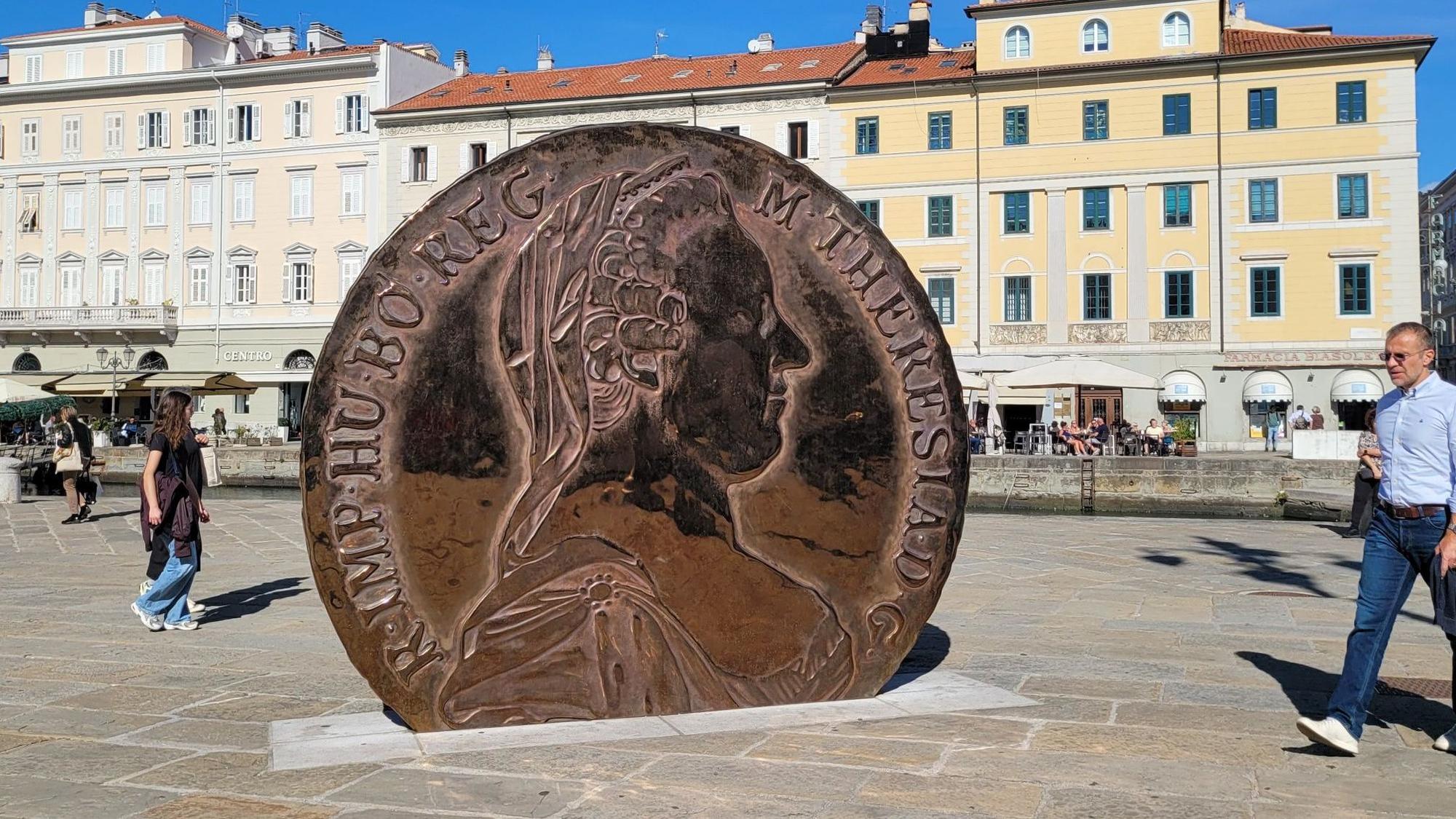 Eine überdimensionale Münze mit dem Konterfei Maria Theresias darauf steht auf einem Platz zwischen alten Häusern