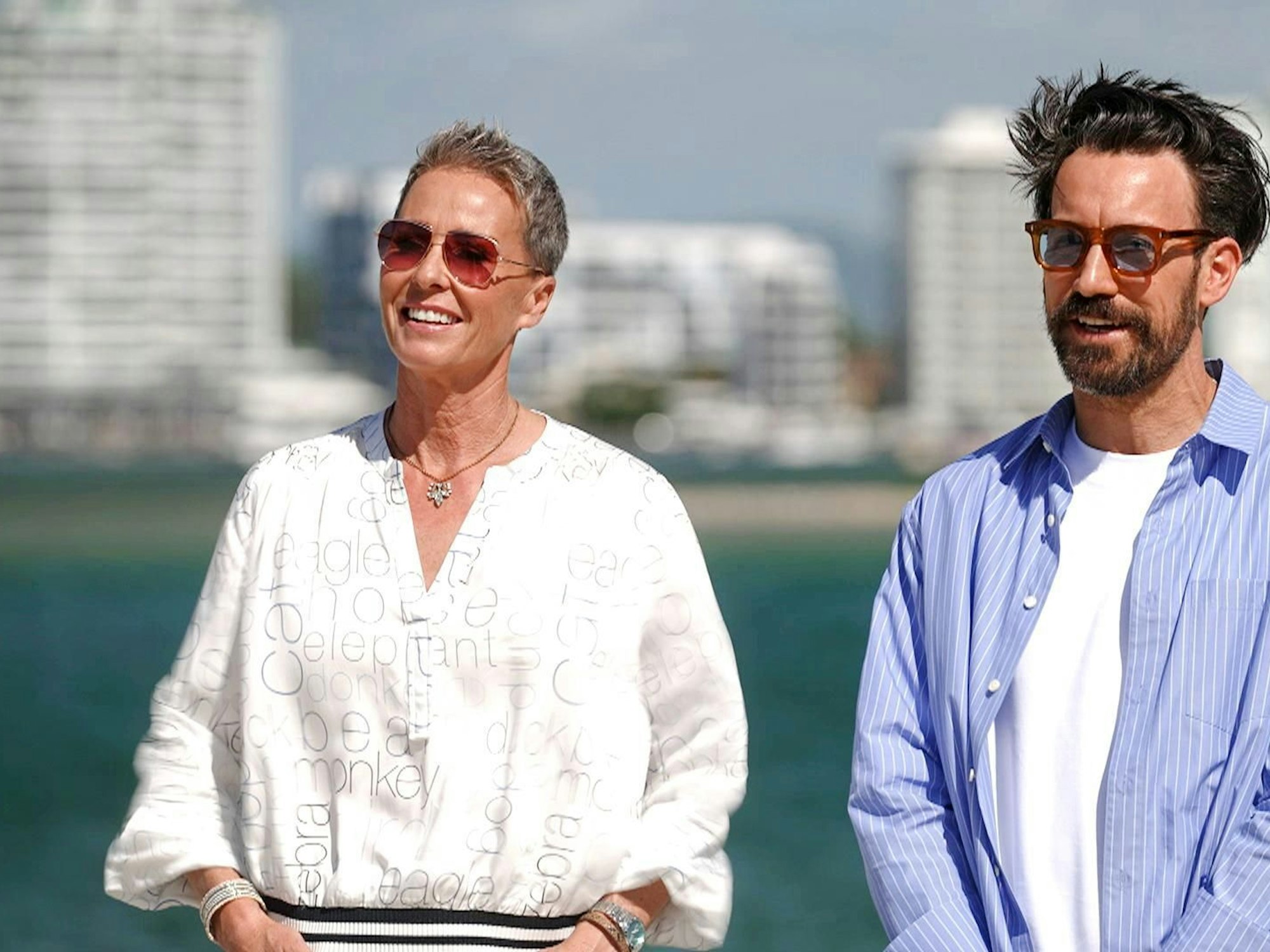 Sonja Zietlow und Jan Köppen lächeln zusammen vor der sonnigen Kulisse. Wie heiß wird es im Camp?