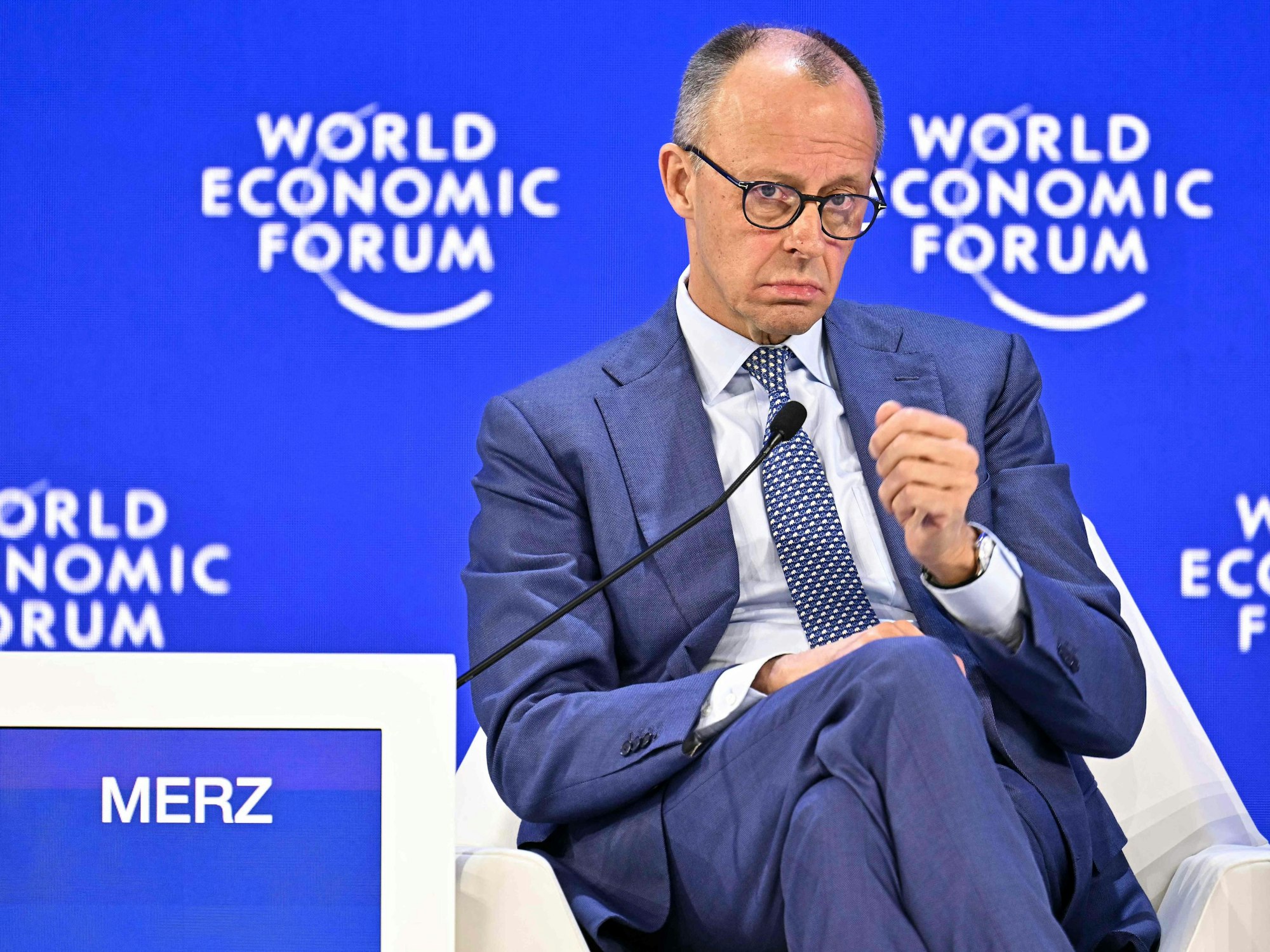 Bundeskanzler Friedrich Merz sitzt vor einem Mikrofon und gestikuliert. Im Hintergrund steht auf einer Wand "World Economic Forum".