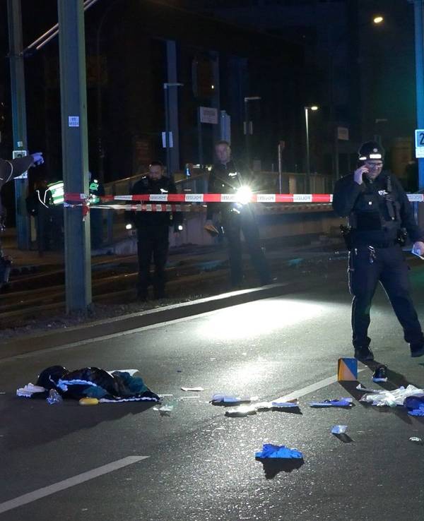 Einsatzkräfte der Polizei untersuchen einen mit Flatterband abgesperrten Tatort auf einer Straße.