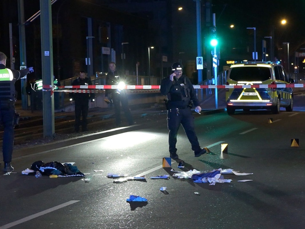 Einsatzkräfte der Polizei untersuchen einen mit Flatterband abgesperrten Tatort auf einer Straße.