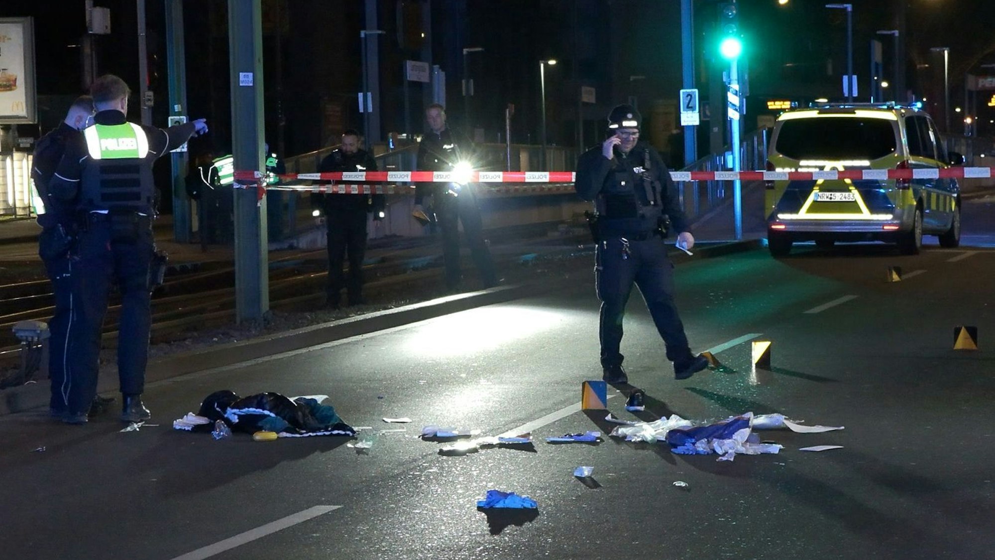Einsatzkräfte der Polizei untersuchen einen mit Flatterband abgesperrten Tatort auf einer Straße.