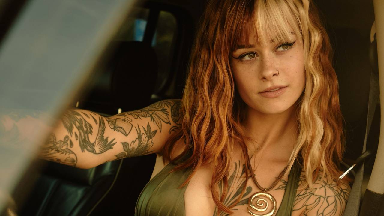 Sally Dinosaur sitzt in einem Auto hinterm Steuer.