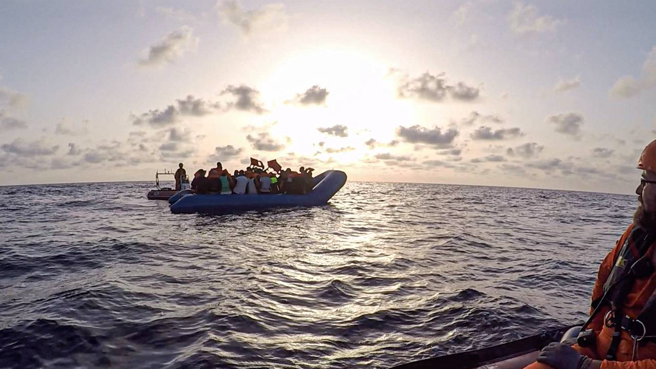 Ein Schlauchboot mit Flüchtlingen treibt auf dem Meer, zwei Seenotretter hat es im Blick.