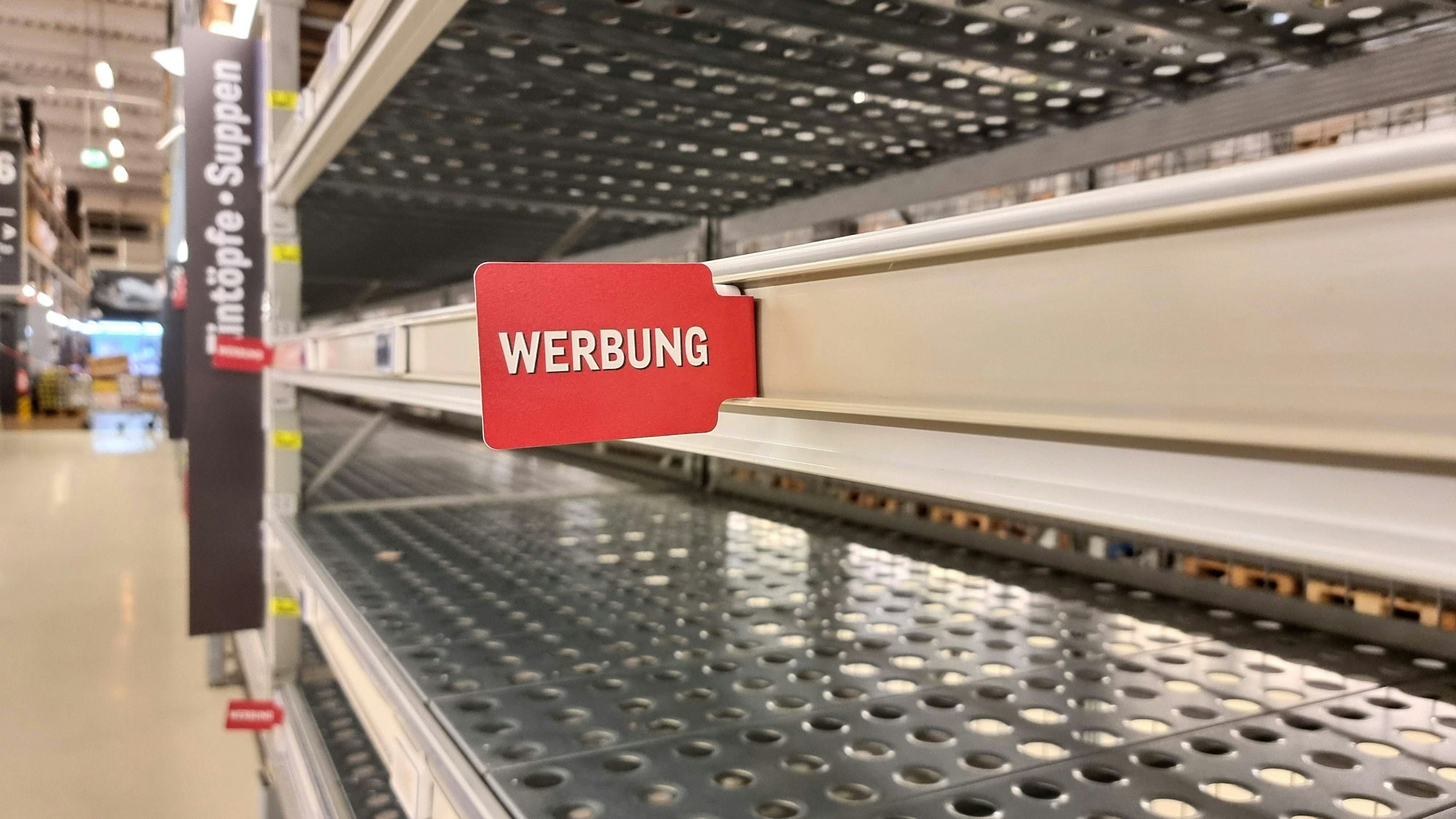Leere Supermarktregale und ein Schild mit Werbung