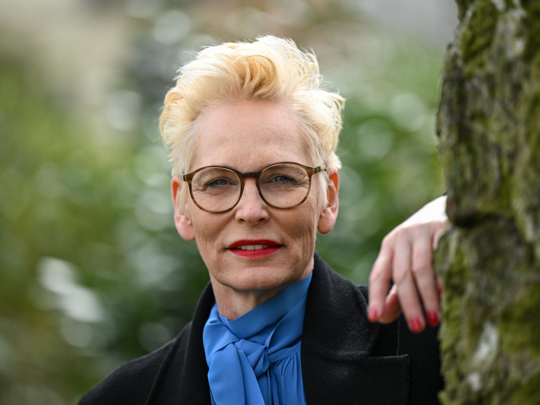 Bärbel Schäfer schaut an einen Baum gelehnt in die Kamera.