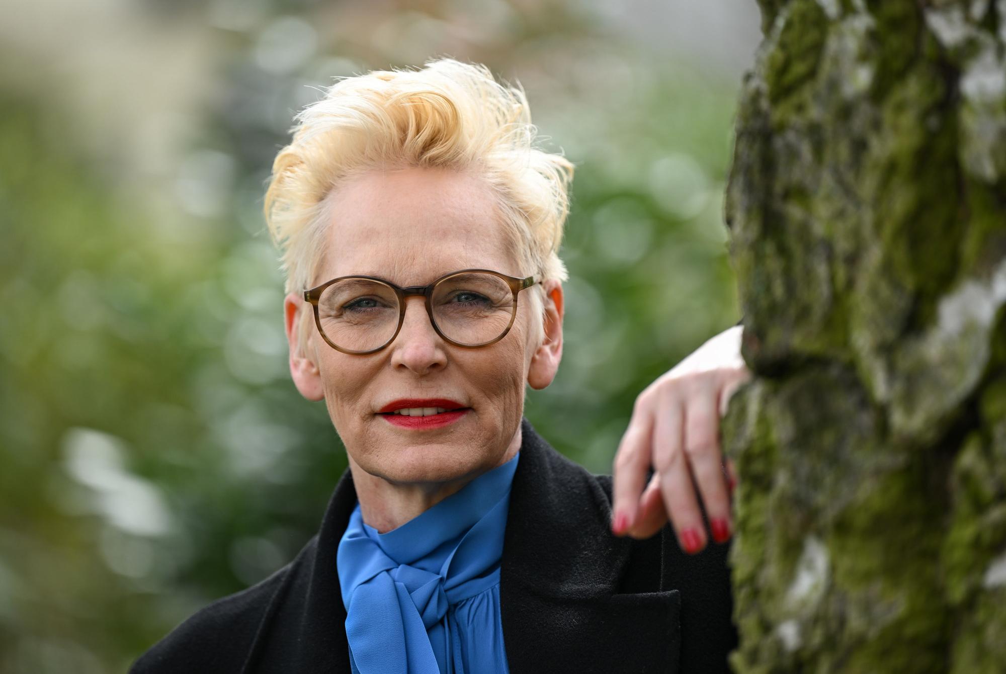 Bärbel Schäfer schaut an einen Baum gelehnt in die Kamera.