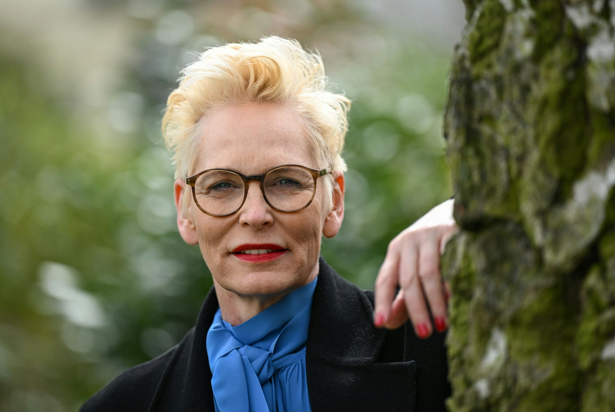 Bärbel Schäfer schaut an einen Baum gelehnt in die Kamera.