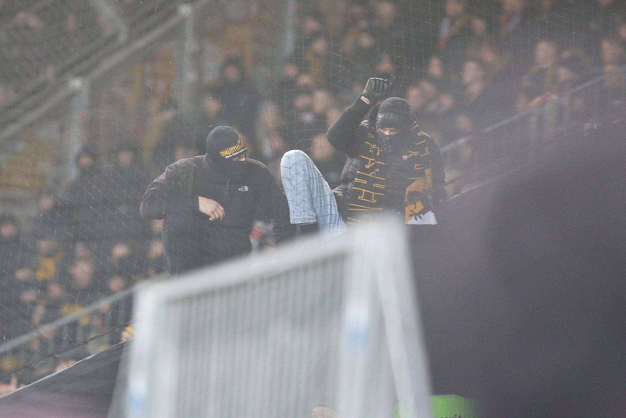 Vermummte Fans von Dynamo Dresden klettern über eine Absperrung.