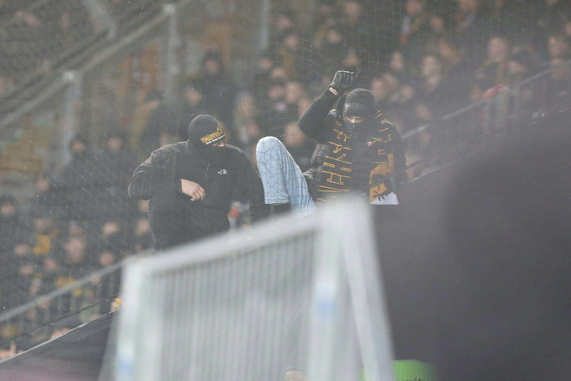 Vermummte Fans von Dynamo Dresden klettern über eine Absperrung.