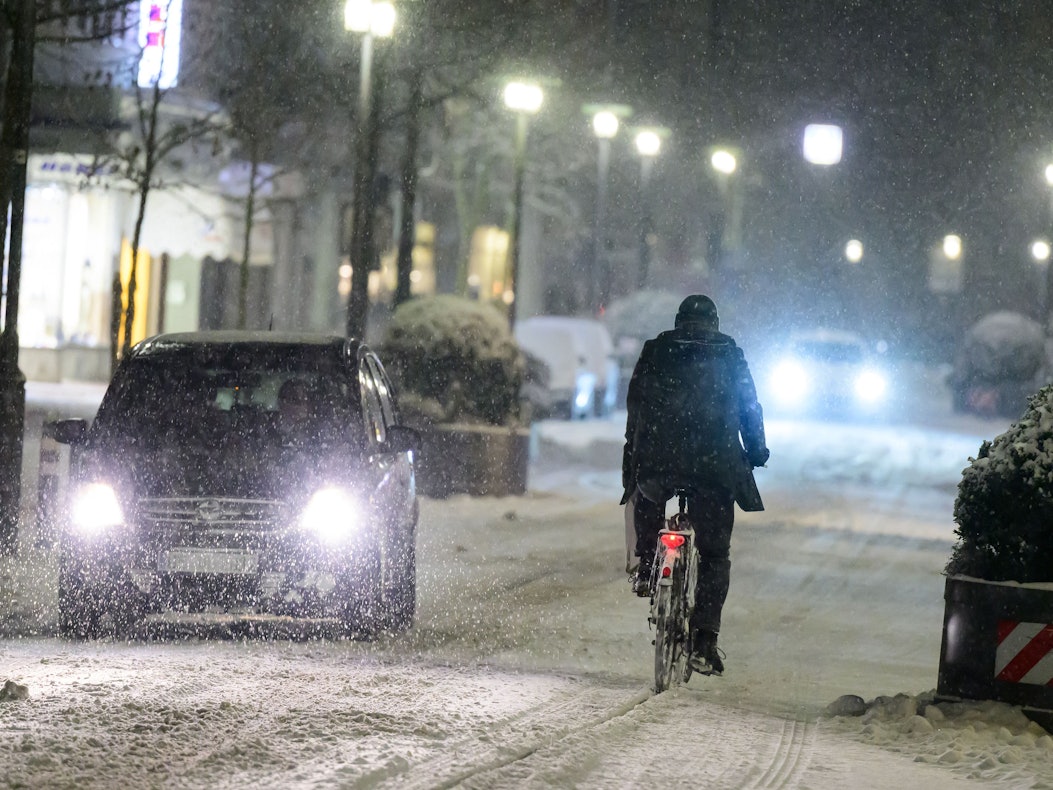 Radfahrer fährt neben Autos über eine schneebedeckte Straße.