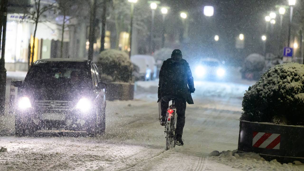 Radfahrer fährt neben Autos über eine schneebedeckte Straße.
