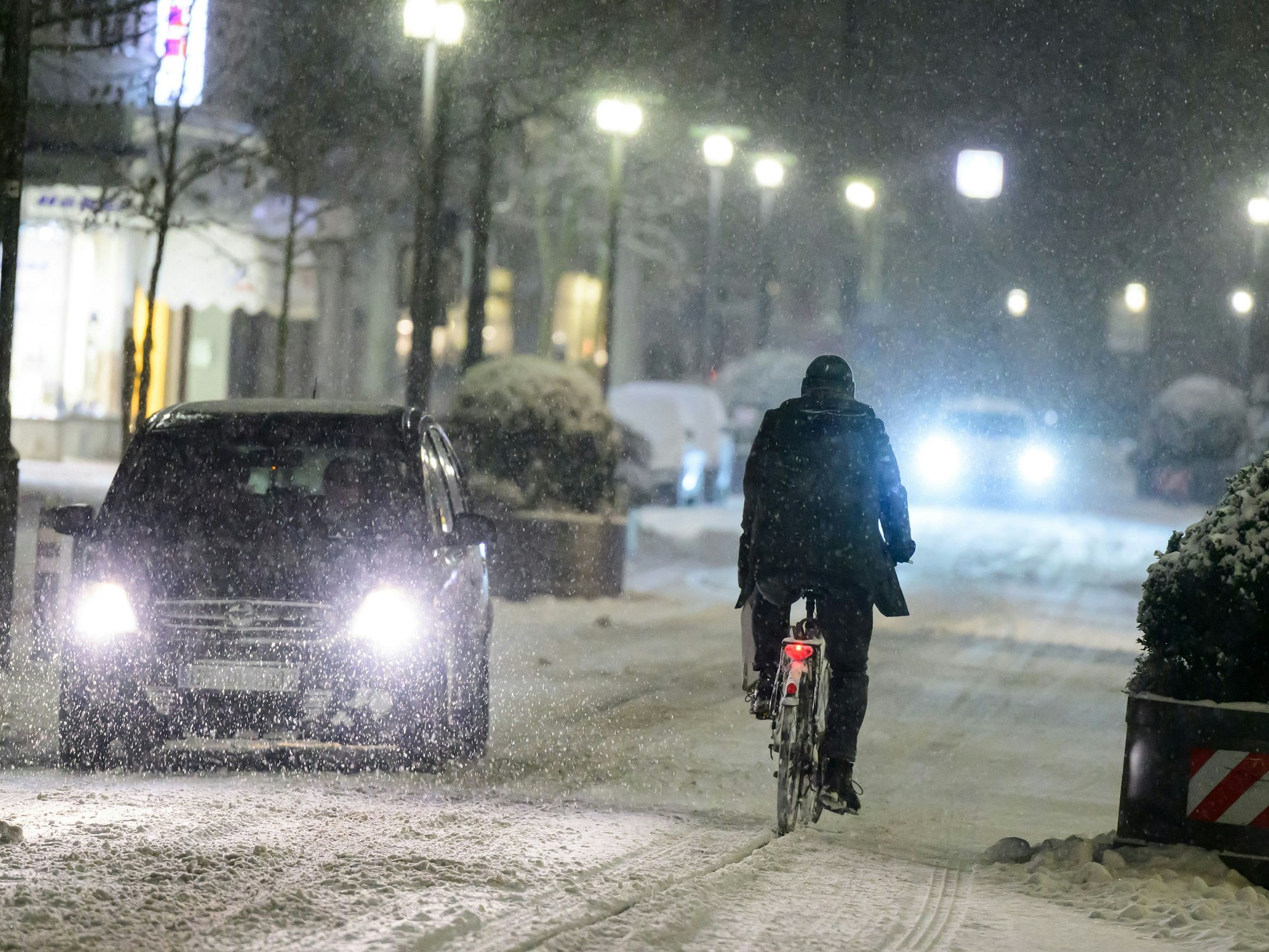 Radfahrer fährt neben Autos über eine schneebedeckte Straße.