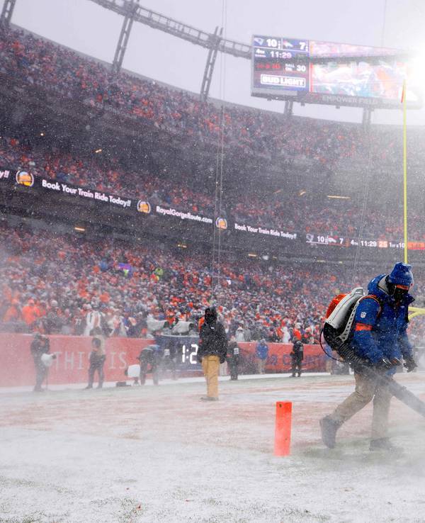 Helfer befreien das Feld im Spiel der Denver Broncos in der NFL von Schnee.